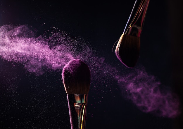 Art of visage. Closeup photo of two professional black make-up brushes with purple powder isolated on black background with copy place.