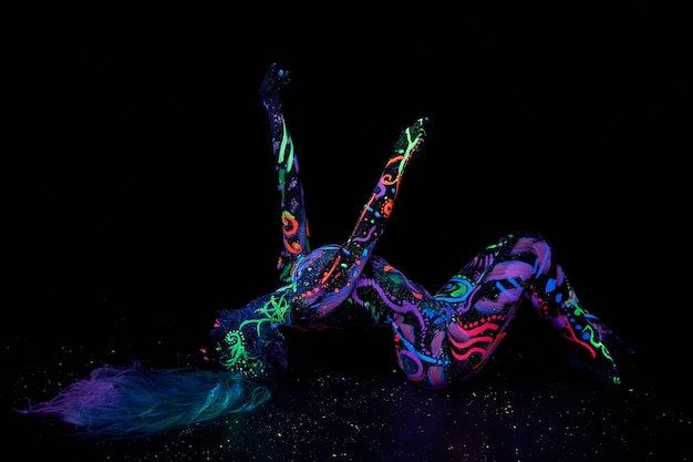 Photo art woman body art on the body dancing in ultraviolet light. bright abstract drawings on the girl body neon color