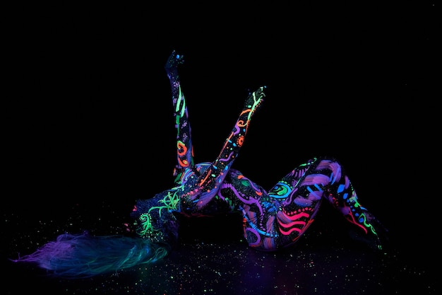 Art woman body art on the body dancing in ultraviolet light.