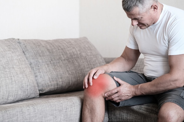 Arthritis is a disease of the joints.A man on a couch, squeezing his knee from excruciating pain.