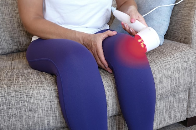 Photo arthritis is a disease of the joints a woman applies a uhf therapy device sitting on the couch to the knee joint