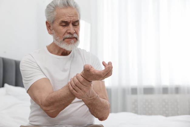 Arthritis symptoms Man suffering from pain in wrist on bed at home space for text