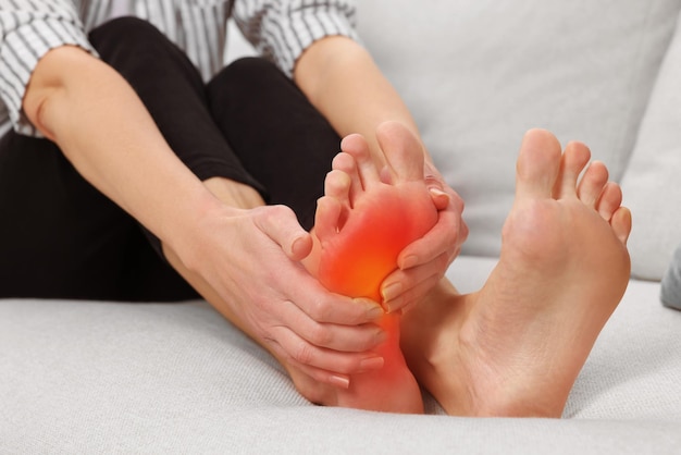 Arthritis symptoms Woman suffering from foot pain on sofa indoors closeup