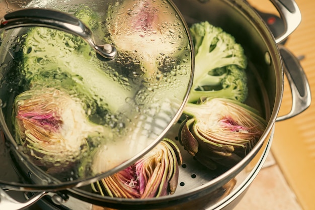 Artichoke purple halves and broccoli in a double boiler Steaming vegetables Vegan healthy food diet concept