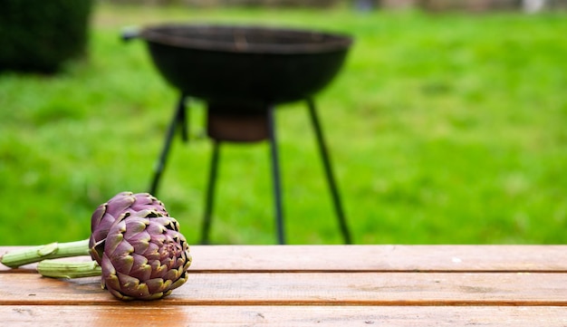 Artichoke on a wooden table outdoors on a blurred grill background Preparing to cook green grill