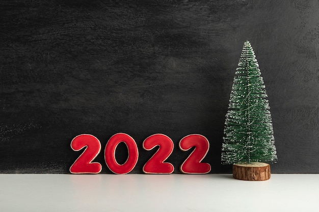 写真 人工的なクリスマスツリーと黒の背景に赤い数字2022。新年のコンセプト。スペースをコピーします。