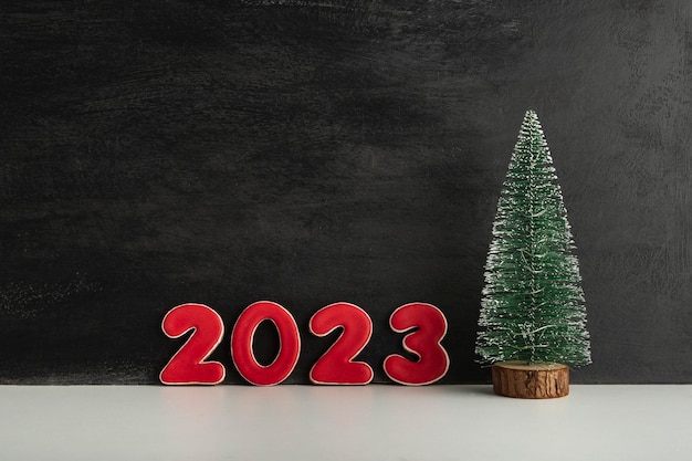 Artificial Christmas tree and red numbers 2023 on black background New year concept Copy space