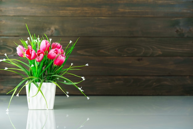 Artificial flower vase bouquet over table with wood wall background