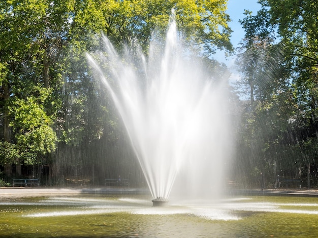 Artificial fountain with reflected bubble water rainbow in natural park under clear blue sky