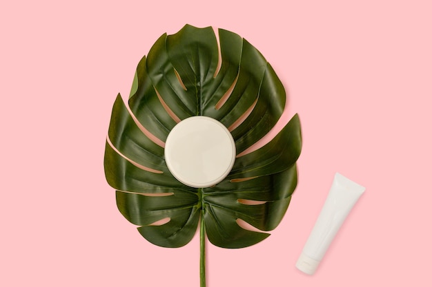Artificial green palm leaf on a pink background Cosmetic cream in a white tube