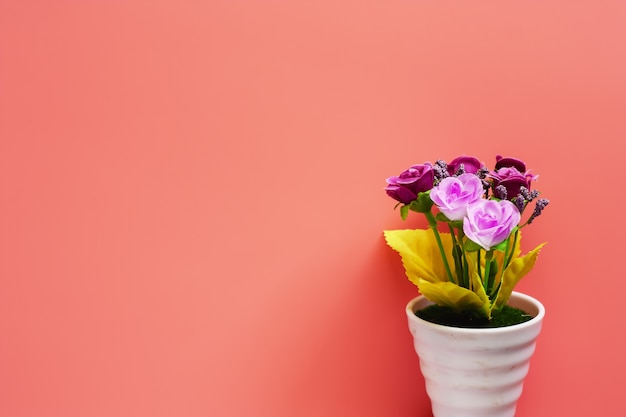 분홍색 배경에 흰색 화분에 인공 분홍색과 보라색 장미 꽃다발