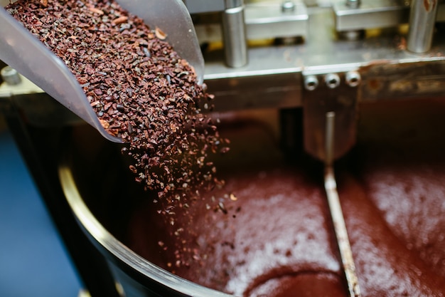 Photo artisan chocolate making, adding cocoa grits in the melanger stone grinder