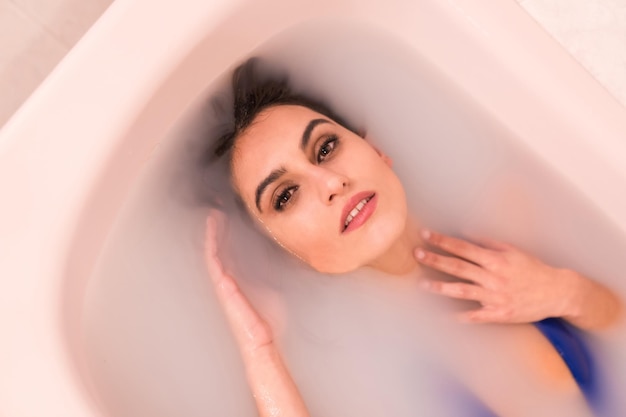 Artisitc portrait from above of a woman on a bath tube in water filled with milk