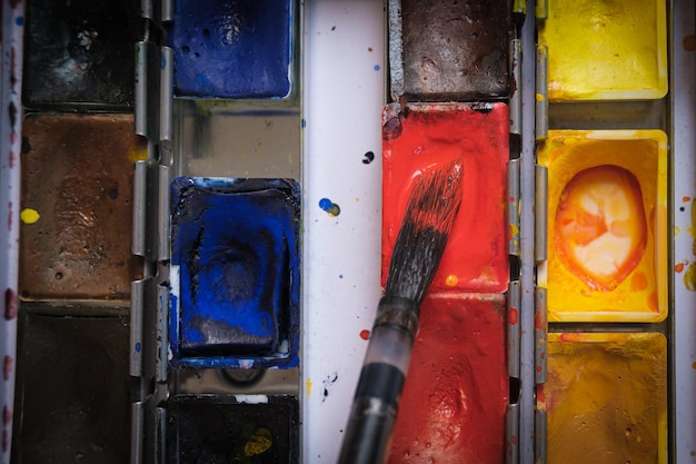 The artist applies red watercolor paint on an art brush