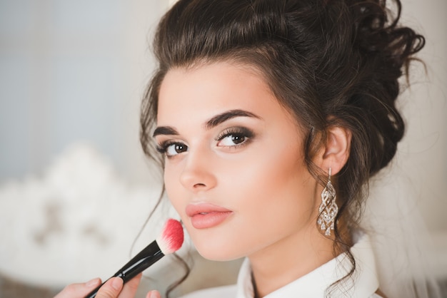 Photo artist applying blush to wedding make up for bride