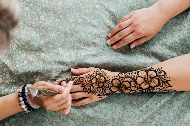 Artist applying floral henna tattoo on women hands design for beauty