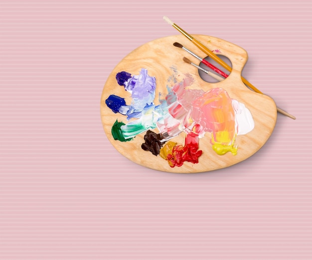 Artist brushes and paint palette on pink background