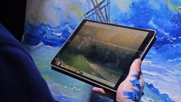 Artist copyist paint seascape with ship in ocean Craftsman decorator draw as boat sail on blue sea with acrylic color In hand of tablet computer pc