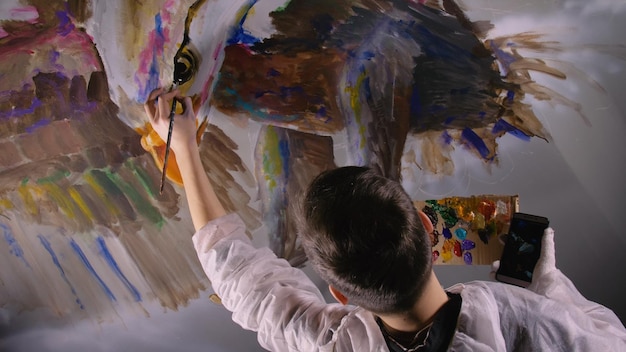 アーティストのデザイナーが壁にワシを描く職人のデコレータがアクリル油絵の具で絵を描く