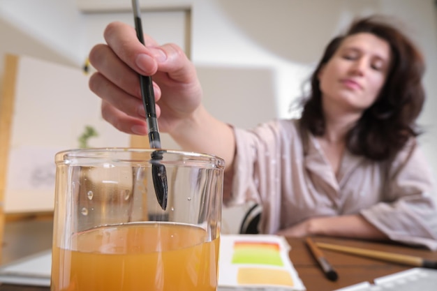 L'artista immerge il pennello artistico in un bicchiere d'acqua. disegnare con gli acquerelli in uno studio d'arte domestico.