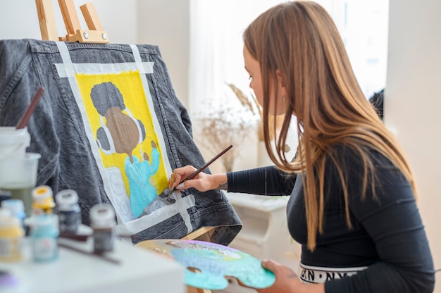 Фото Художник рисует модное искусство на джинсовой куртке мастерская солнечного портного акриловыми красками и мольбертом