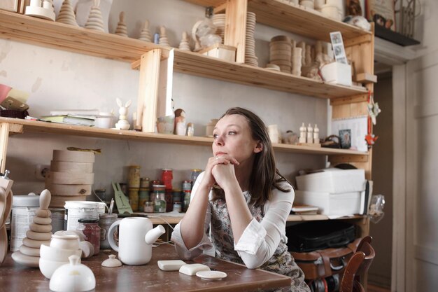 The artist girl is sitting at the table in the studio looking out the window