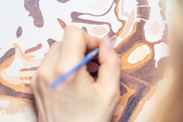 artist hand holds a brush and paints a picture on canvas, close-up