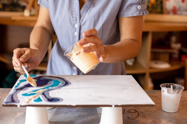 L'artista tiene una tazza di vernice nella mano sinistra e un cucchiaio nella destra, con cui applica la vernice sulla tela.masterclass. creatività e design. l'artista al lavoro. libertà e ispirazione.