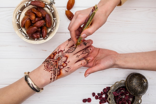 Artista che fa il mehndi sulla mano della donna vicino alla frutta secca dei datteri