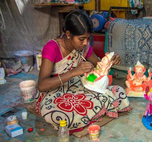 Foto artista che fa una statua e dà il tocco finale a un idolo del dio indù lord ganesha in un laboratorio di artisti per il festival di ganesha