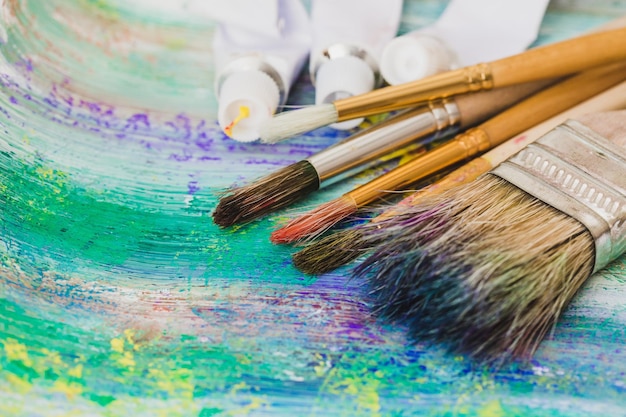 Artist paint brushes and paint tubes of paint over bright watercolor background