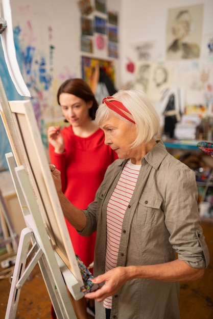 Artist painting. Aged famous blonde-haired artist painting near her dark-haired student