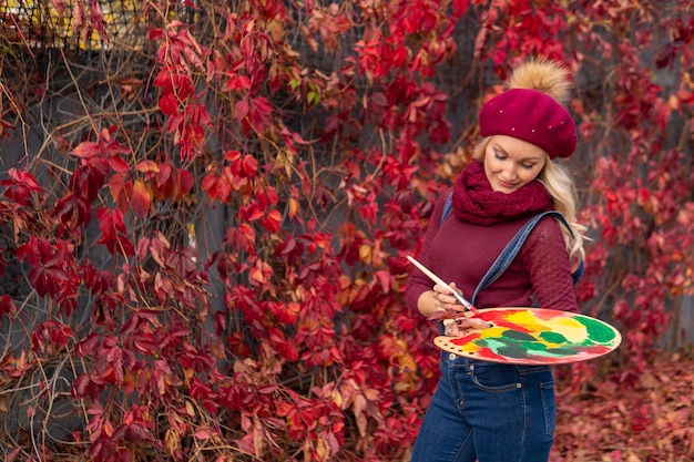 The artist paints red maple leaves on the leaves with red\
paints in blue jeans and a burgundy