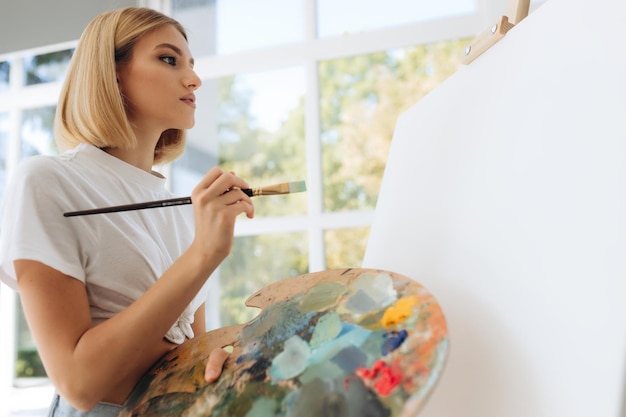 L'artista dipinge in studio ragazza attraente che indossa una maglietta bianca