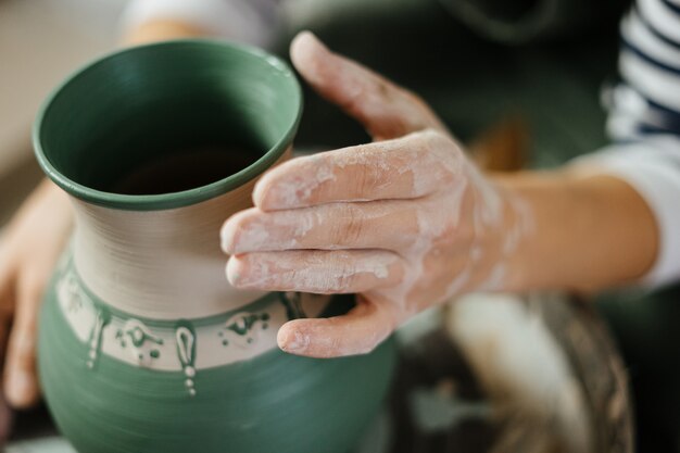 Artist's hand next to painted handmade pot at ceramic workshop. Pottery. Ceramic skills.