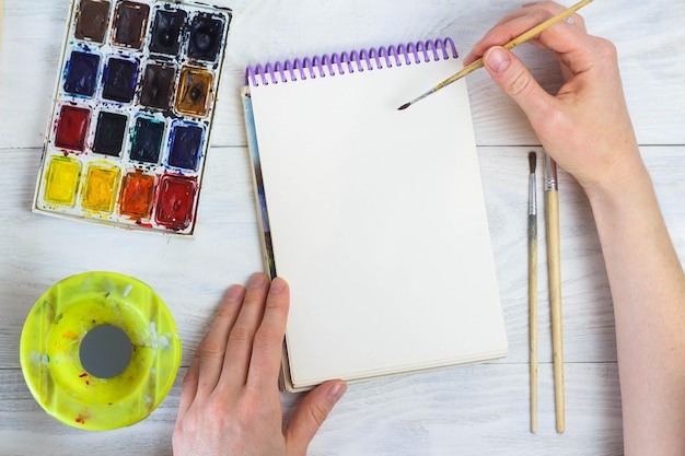 The artist's hands paint palette brushes different colors The girl is drawing The artist's tools for real art and inspiration Top View