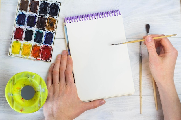 The artist's hands paint palette brushes different colors The girl is drawing The artist's tools for real art and inspiration Top View