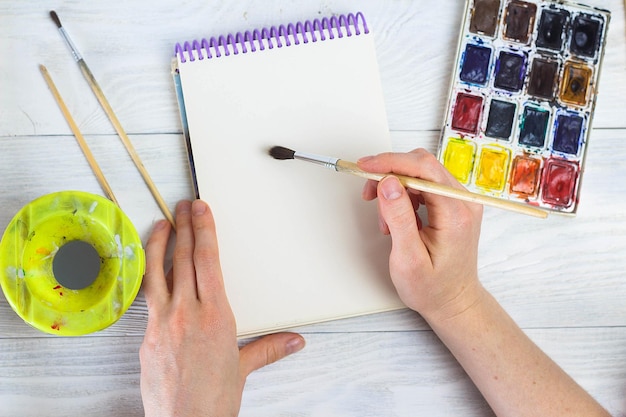 The artist's hands paint palette brushes different colors The girl is drawing The artist's tools for real art and inspiration Top View