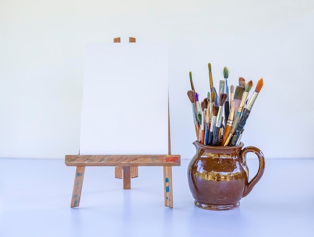 Artist\'s workplace canvas on the wooden easel and brushes in\
ceramic jug