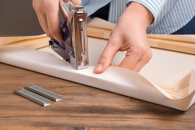 The artist stretches the canvas on a wooden frame with a stapler