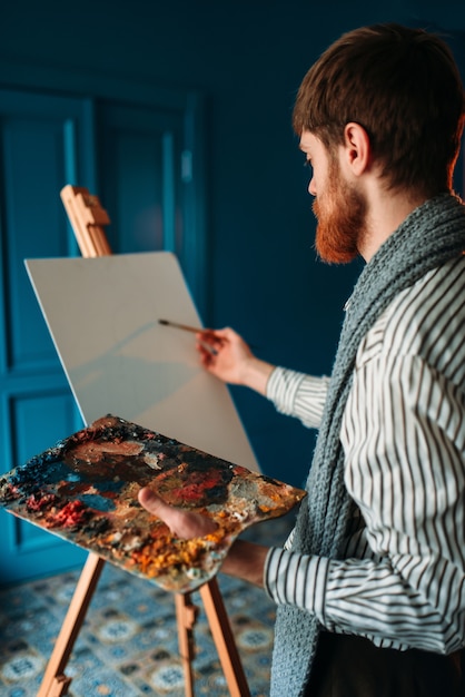 Photo artist with palette and brush in front of easel