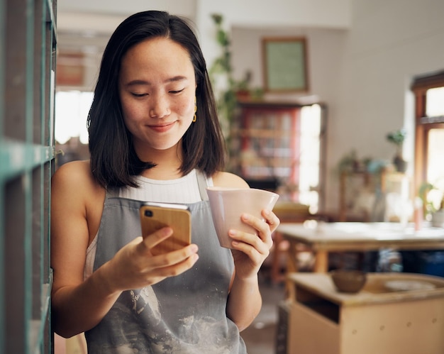 Photo artist woman phone and reading chat with coffee smile and focus on email app or social media for date asian art entrepreneur social network and smartphone with happiness tea and relax in studio