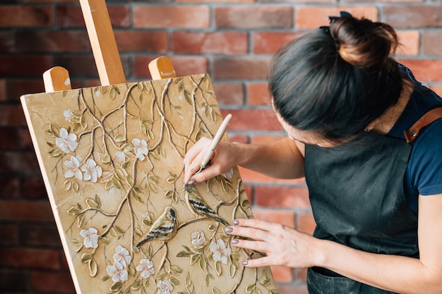 Photo artist at work. studio workspace. woman painter with palette knife. art painting canvas on easel. birds and flowers.