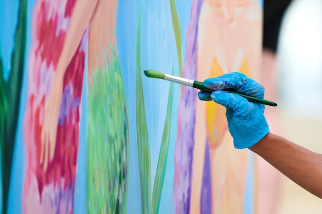 Artist39s hand met penseel schilderen kleurrijke foto op canvas op openlucht kunstfestival Vrouw schilder in blauwe handschoenen trekt surrealistisch beeld met penseel mooie kunstprestaties