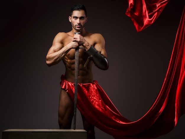 Artistic image with naked muscular man in a red fluttering dress.