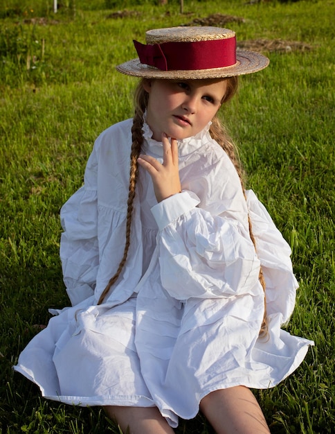 Artistic photo of a girl with pigtails and a hat sitting on the grass