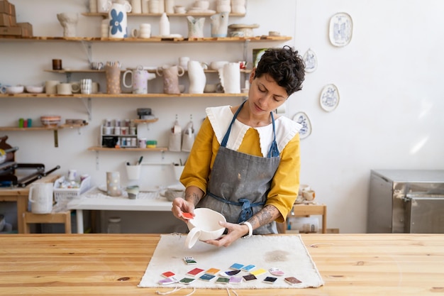 Foto donna artistica sceglie il colore per la pittura di coppe di ceramica artigianale produzione di stoviglie e piccole imprese