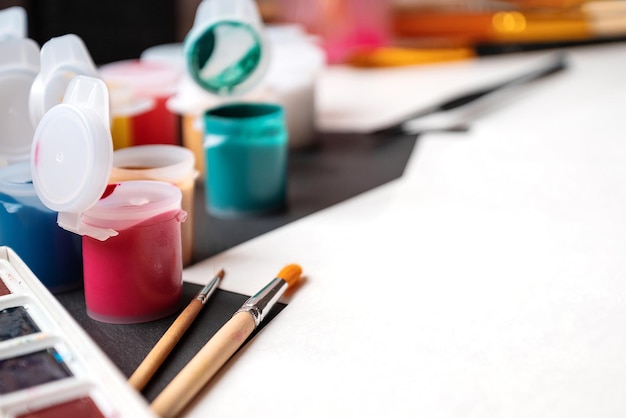 Photo artistic work desk with plastic gouache paint cans paint brushes and paper ready to draw