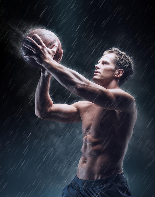 Artistiek portret van shirtless natte bascetballspeler onder druppeltjes.