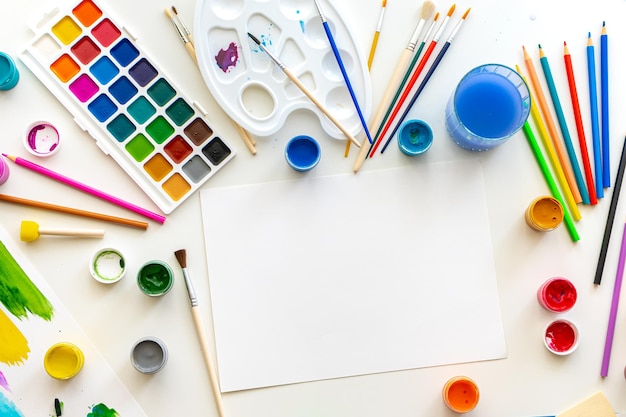 The artists workplace at the drawing lesson a white sheet of paper surrounded by colorful paints and